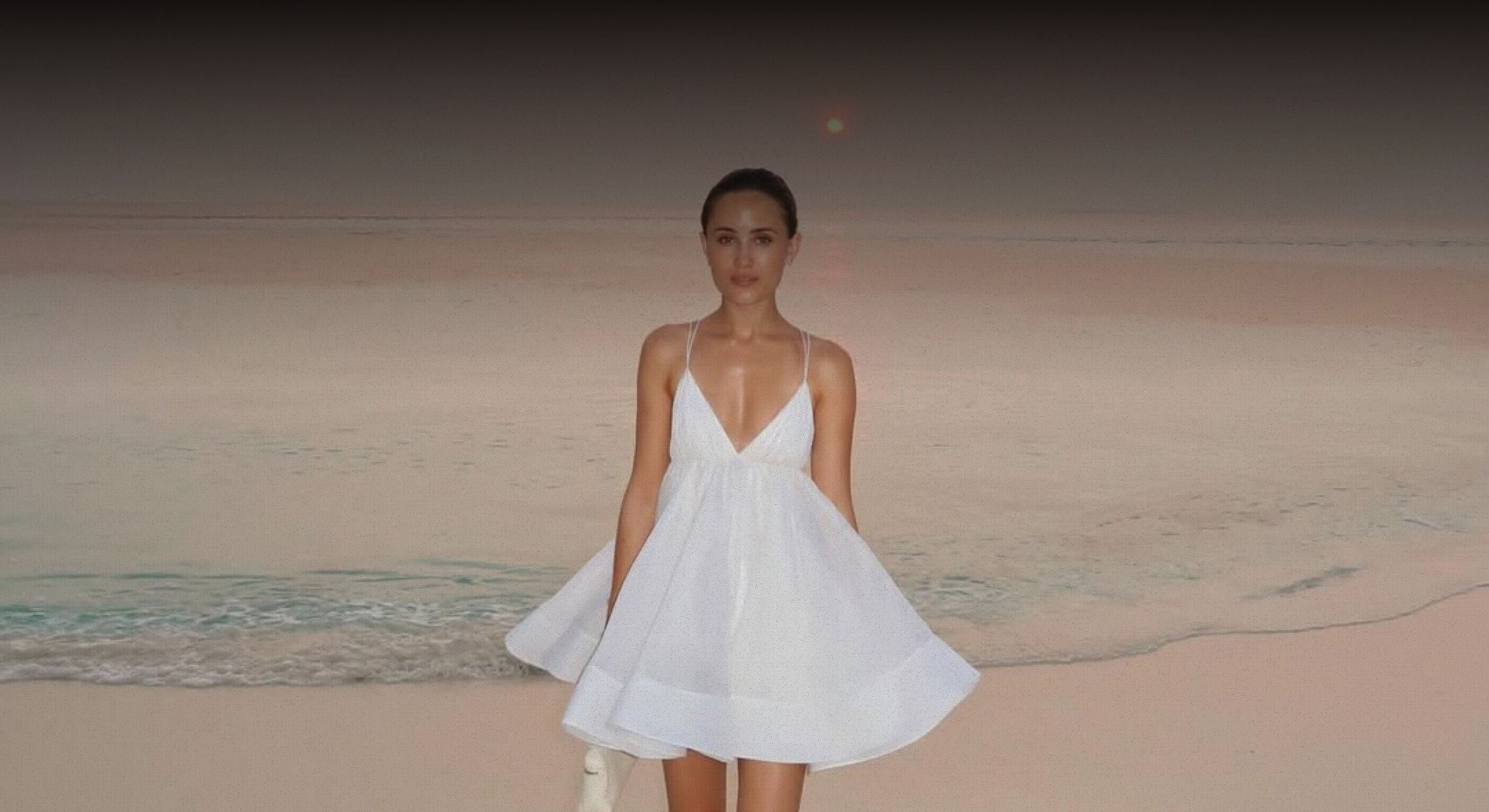 Woman in a white dress standing on a beach with a minimalistic background