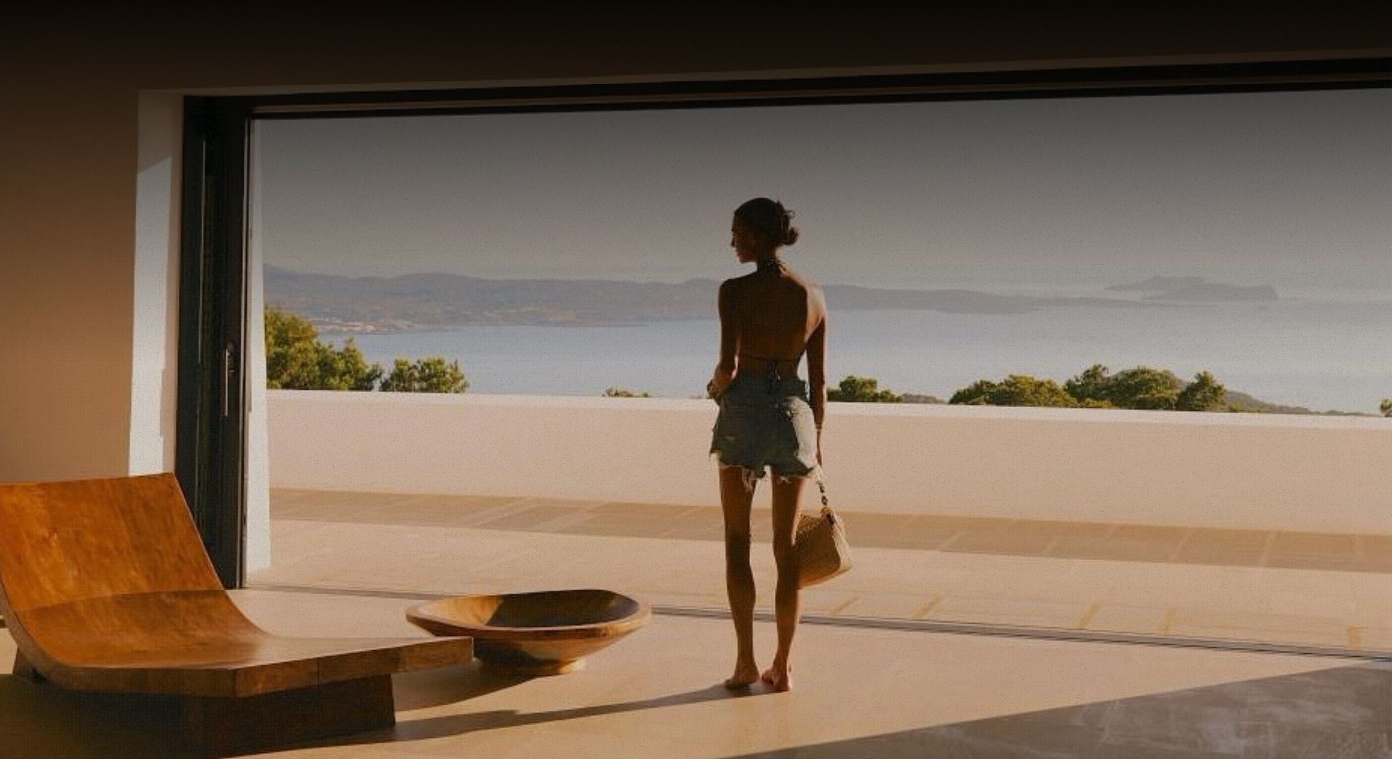 Woman standing on a terrace overlooking a scenic view with a modern interior.