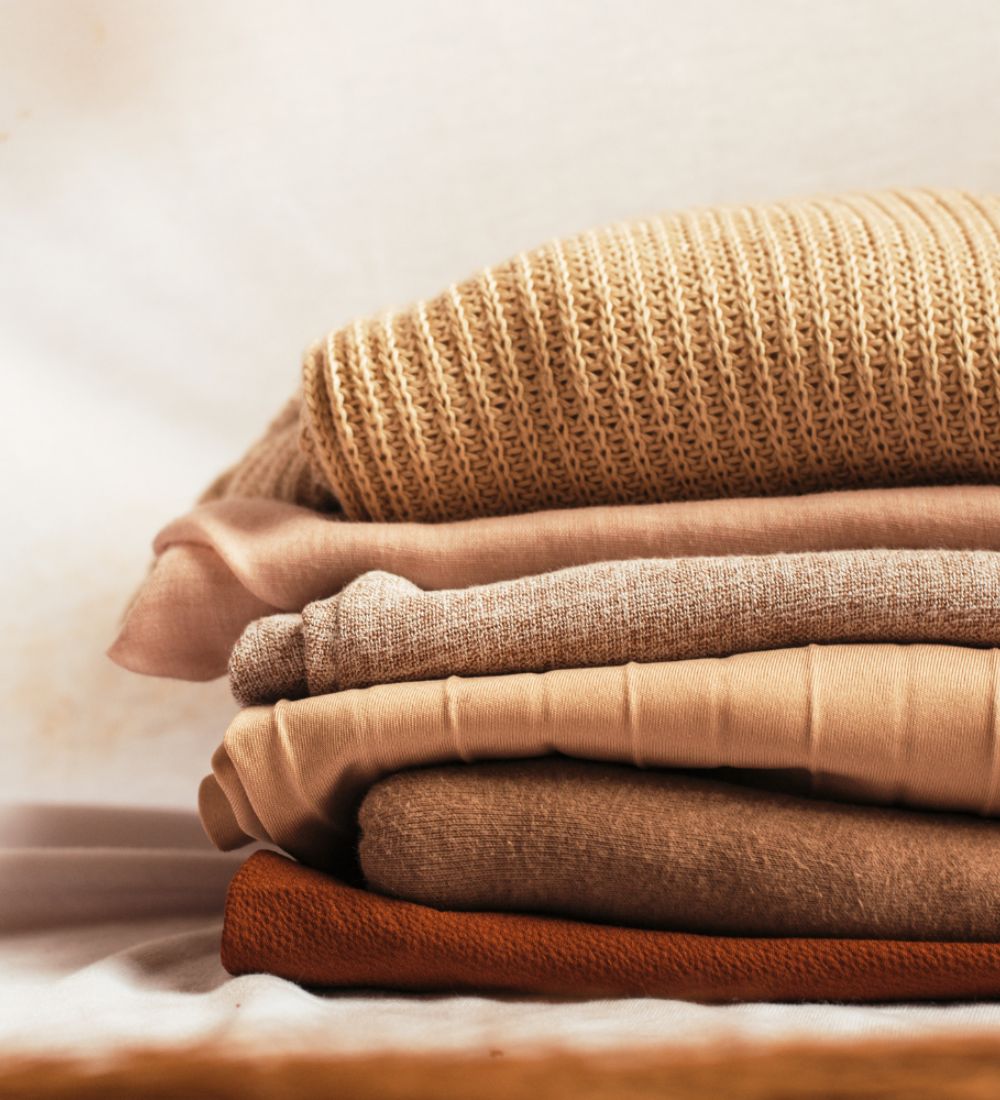Stack of folded brown and beige sweaters on a light background