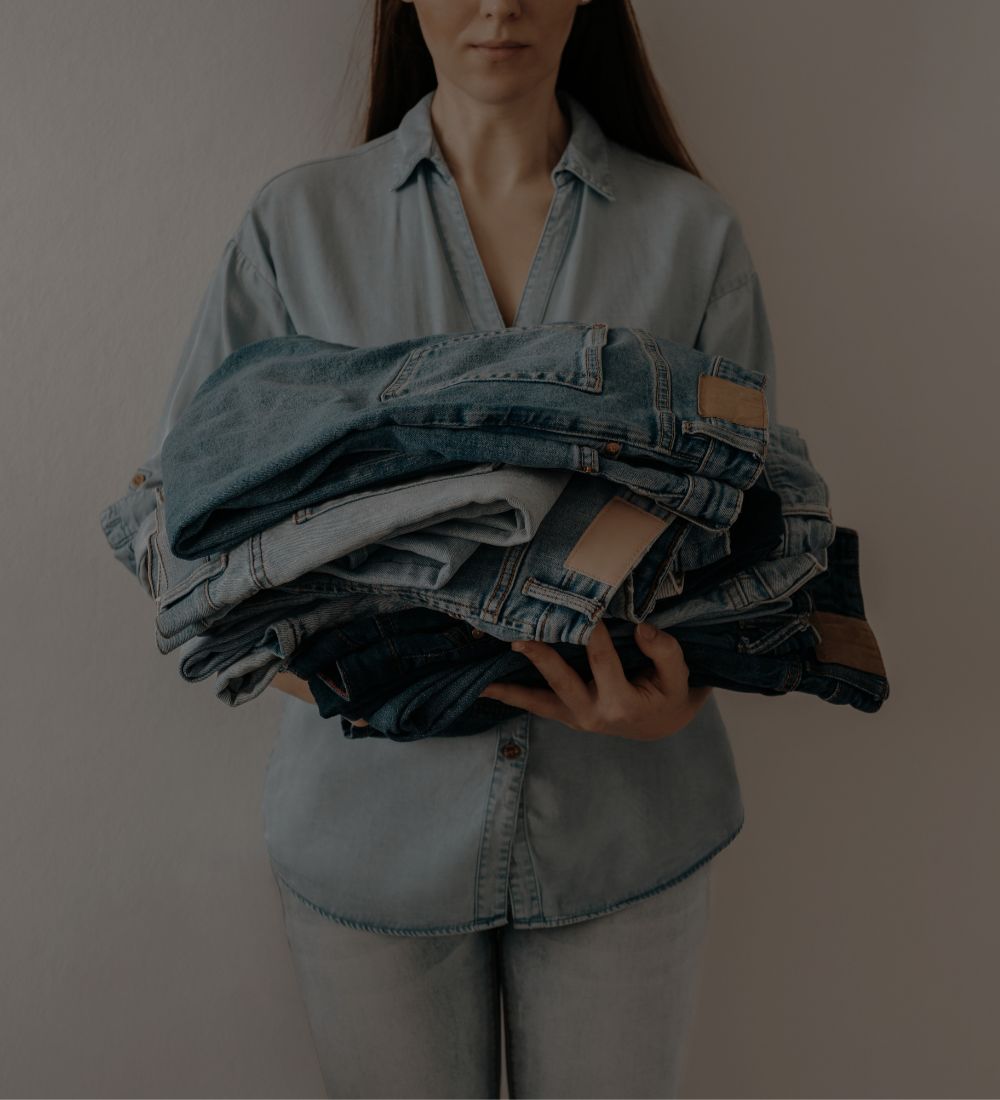 Person holding a stack of denim jeans against a plain background