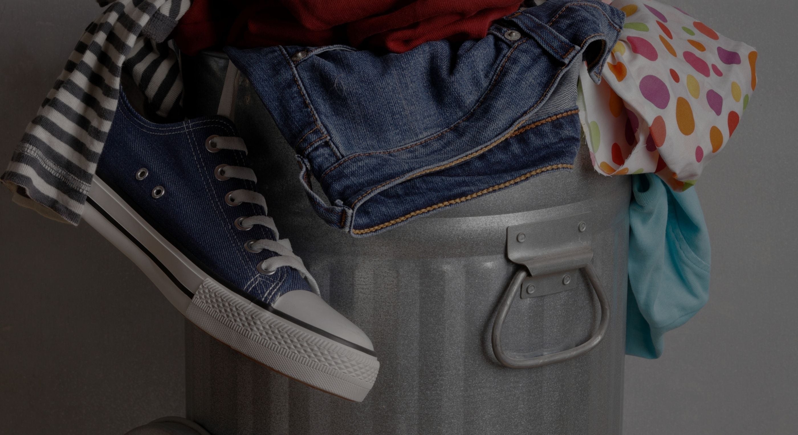 Garbage bin filled with clothes and shoes on a dark background