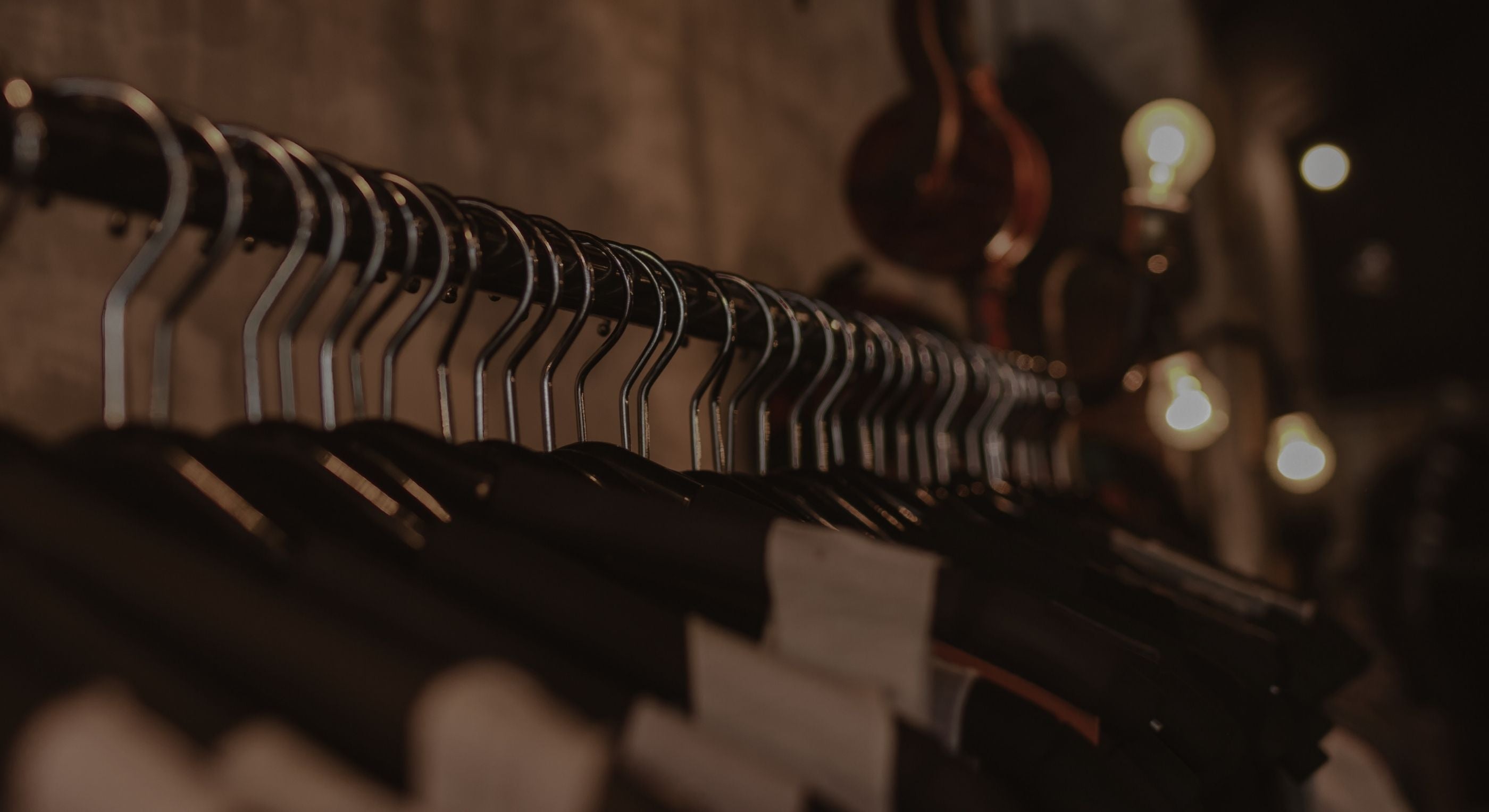 Row of black hangers on a rack with a warm, blurred background