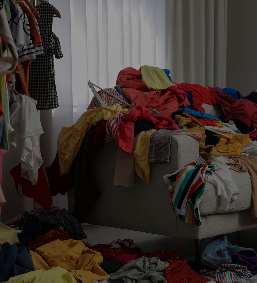 Cluttered room with clothes scattered on a couch and floor.