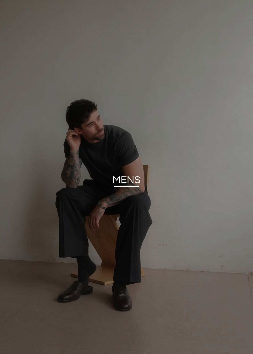 Man sitting on a chair against a plain wall with 'MENS' text overlay.