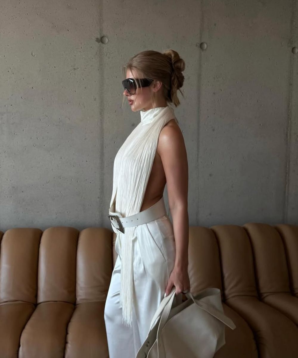 Woman in a white outfit standing in a room with a brown couch and concrete wall.