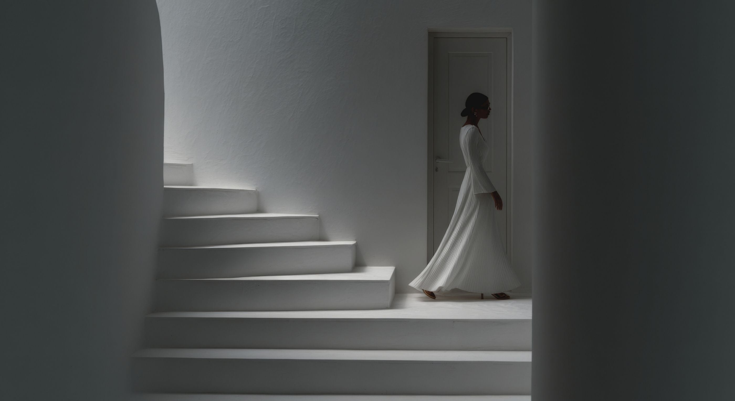 Woman in a white dress standing at the top of a white staircase in a minimalistic setting