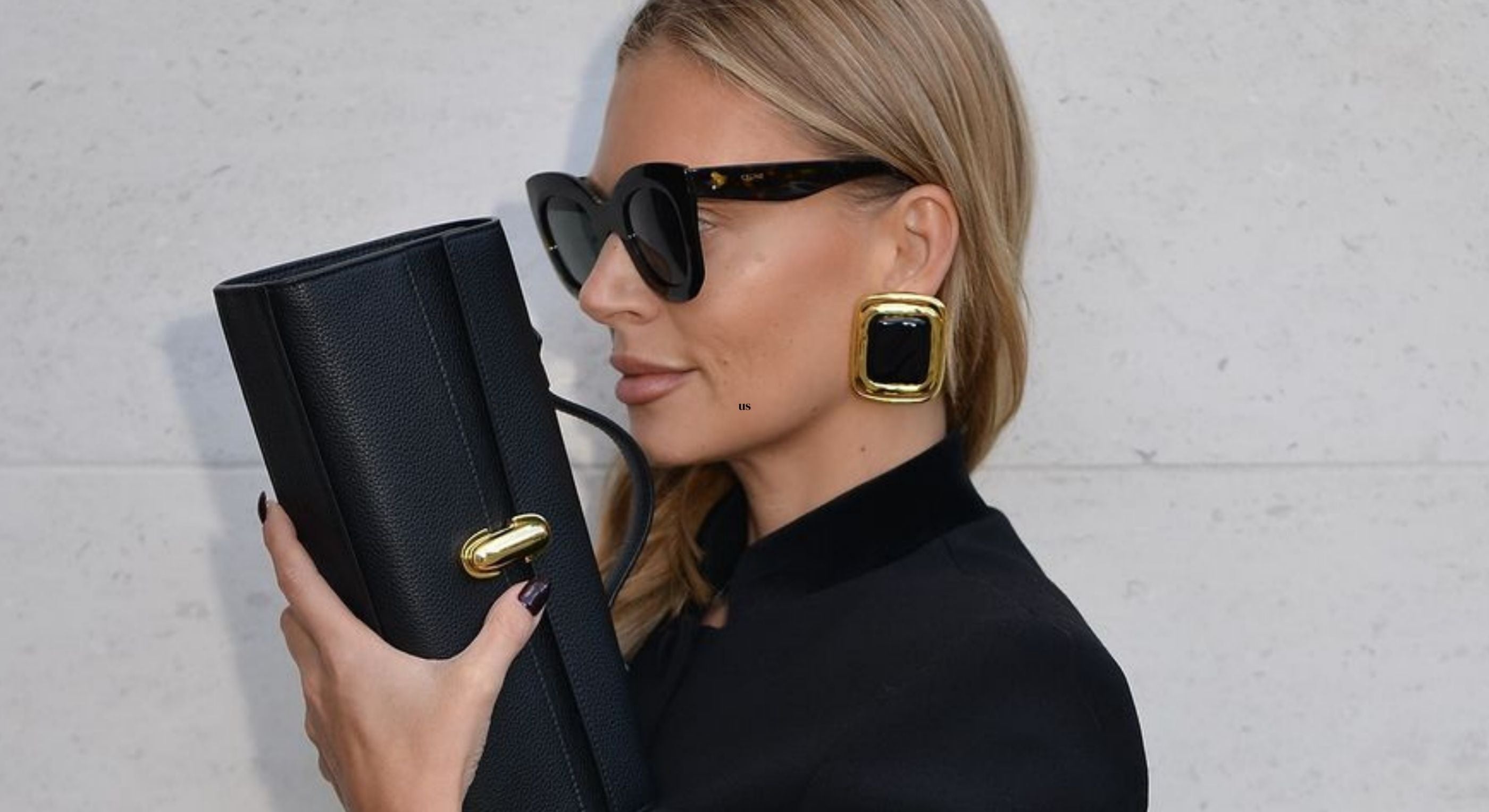 Woman holding a black handbag with gold accents against a light gray background