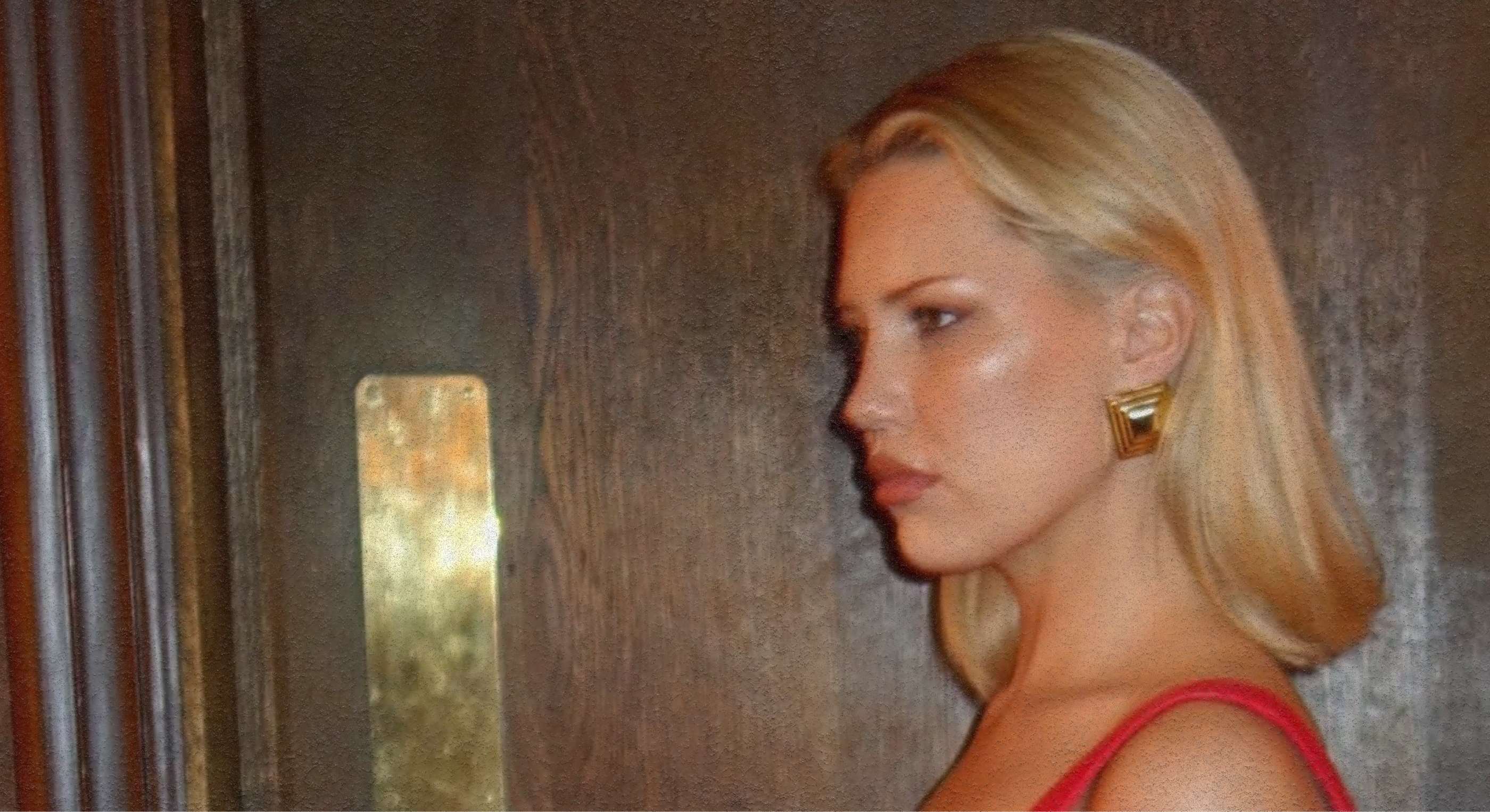 Woman with blonde hair and a red dress standing in front of a textured wall.