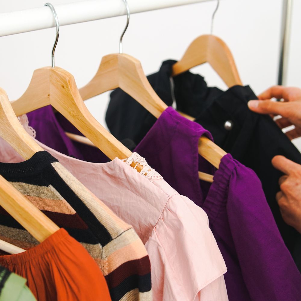 Colorful clothing on hangers with a person's hand selecting an item.