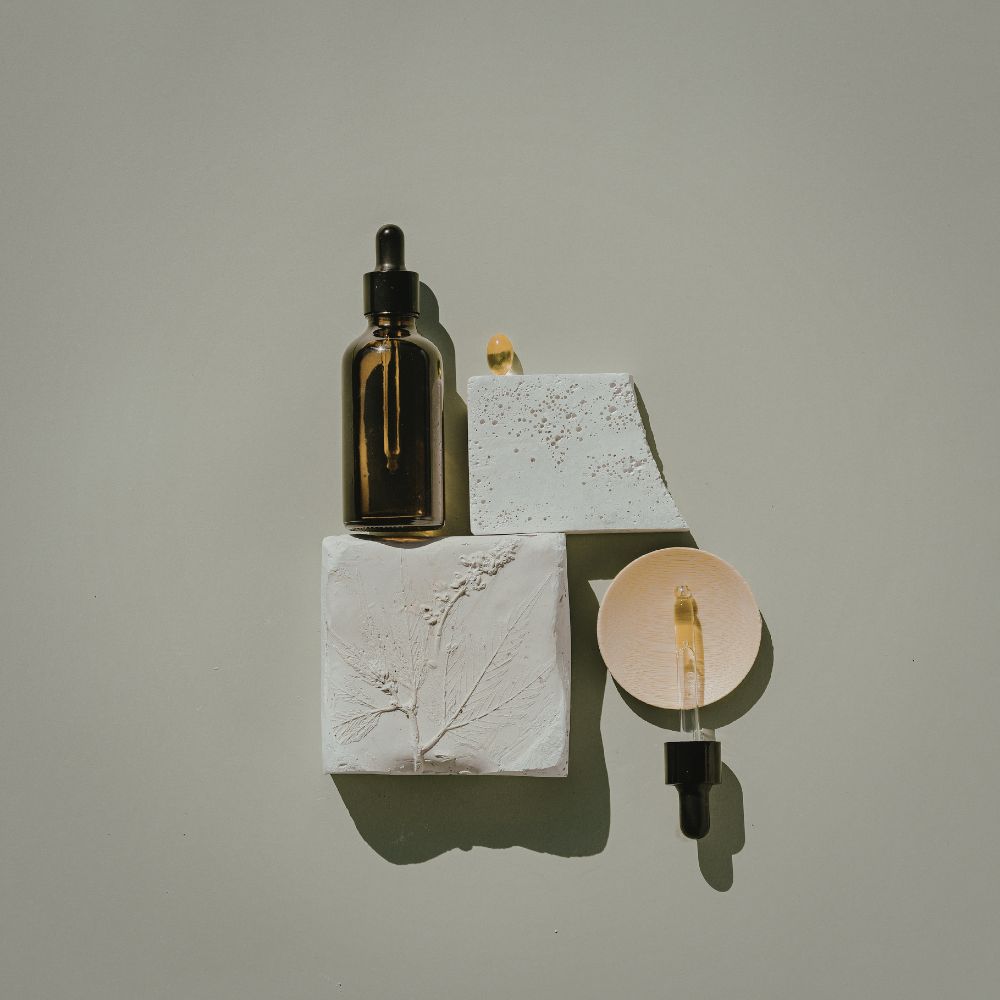 Two glass bottles with droppers on textured white blocks against a neutral background