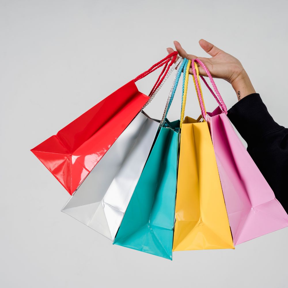 Hand holding five colorful shopping bags on a light gray background